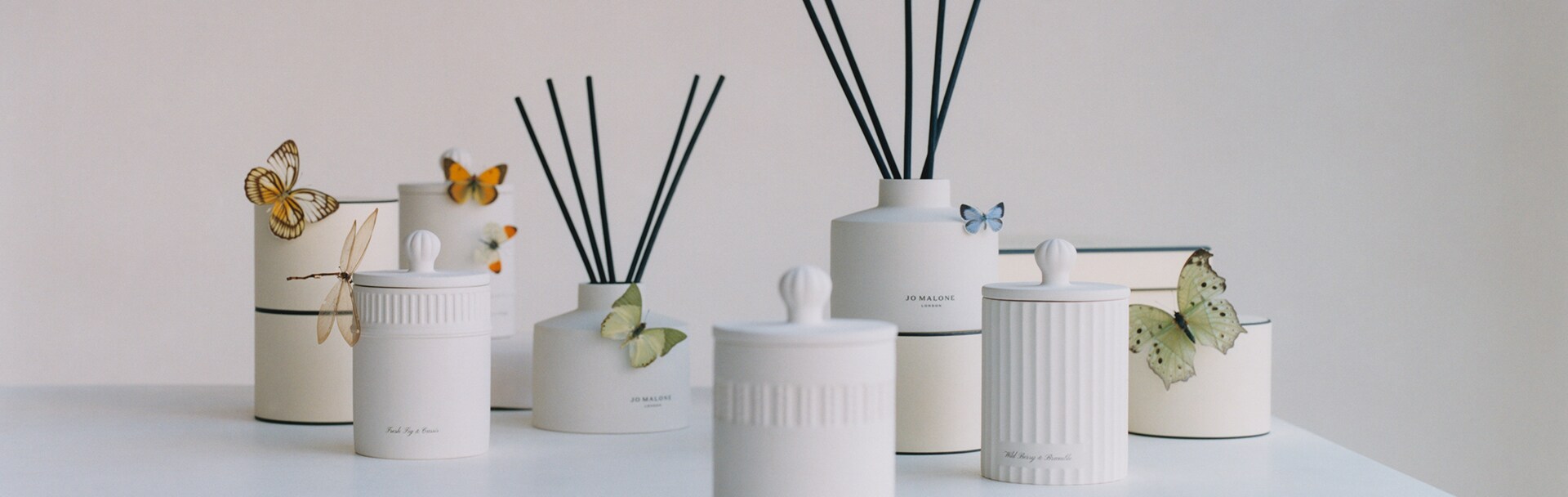 Image de diffuseurs et bougies de la Collection Townhouse Jo Malone, survolés par des papillons et une libellule